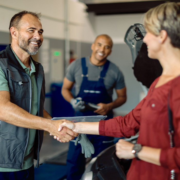 A man and woman shaking hands in front of a car, symbolizing a successful business deal.