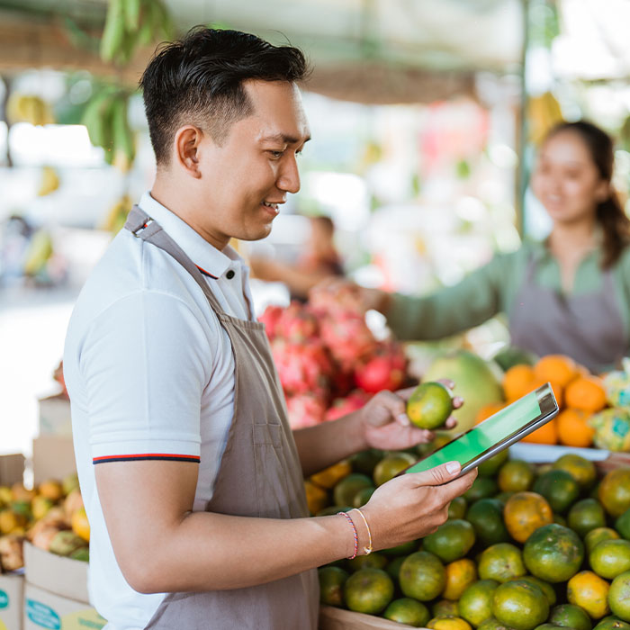 An Asian man carefully examines produce at an Irish market using a tablet device