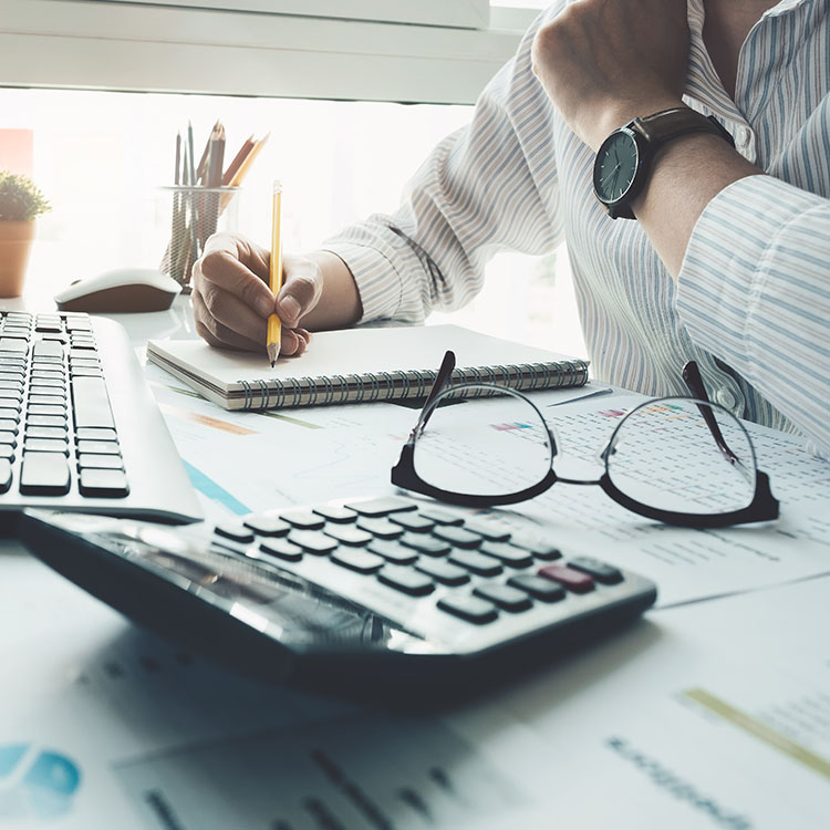 A focused businessman at his desk, using a calculator and pen to work on financial calculations