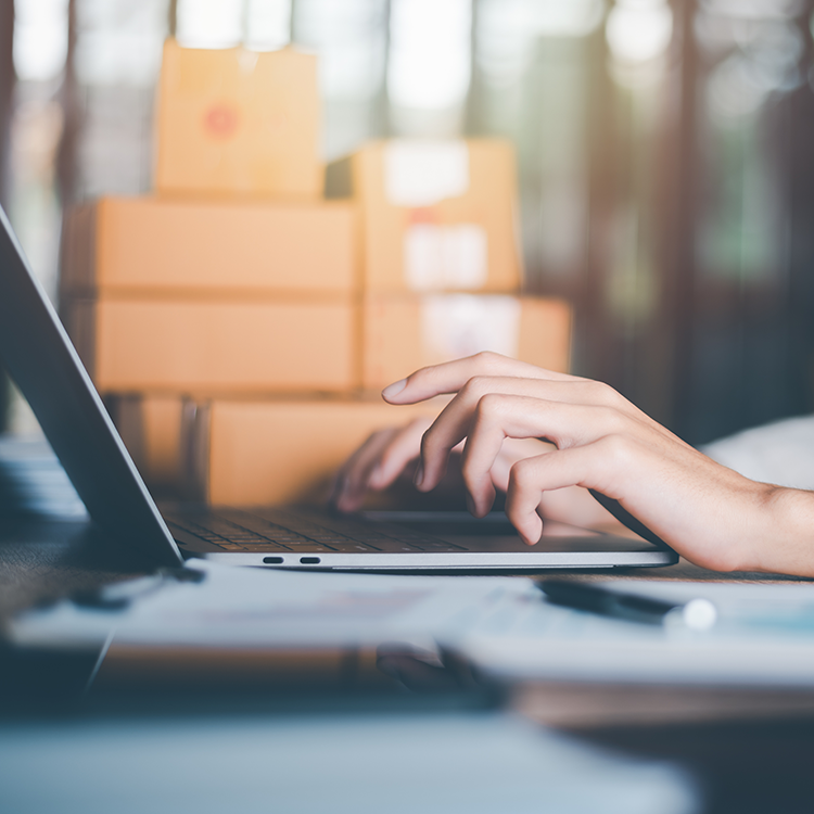 A person typing on a laptop surrounded by stacked boxes on a table.