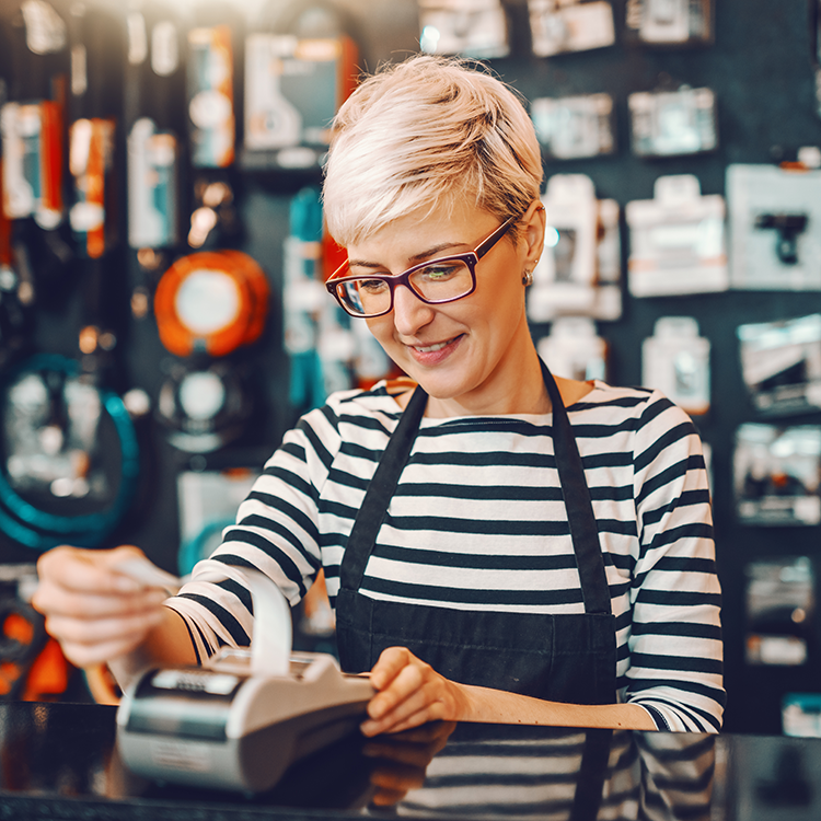 A woman with glasses happily uses a credit card for a purchase, displaying a genuine smile.