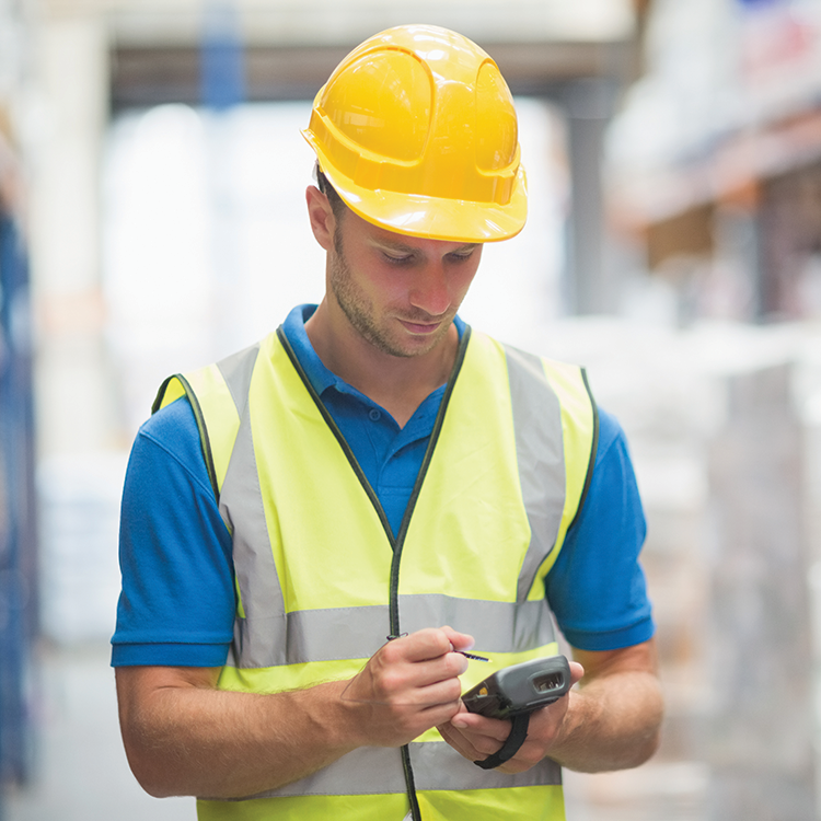 An Irish warehouse employee, wearing a hard hat and vest, utilizes a mobile device to efficiently manage stock