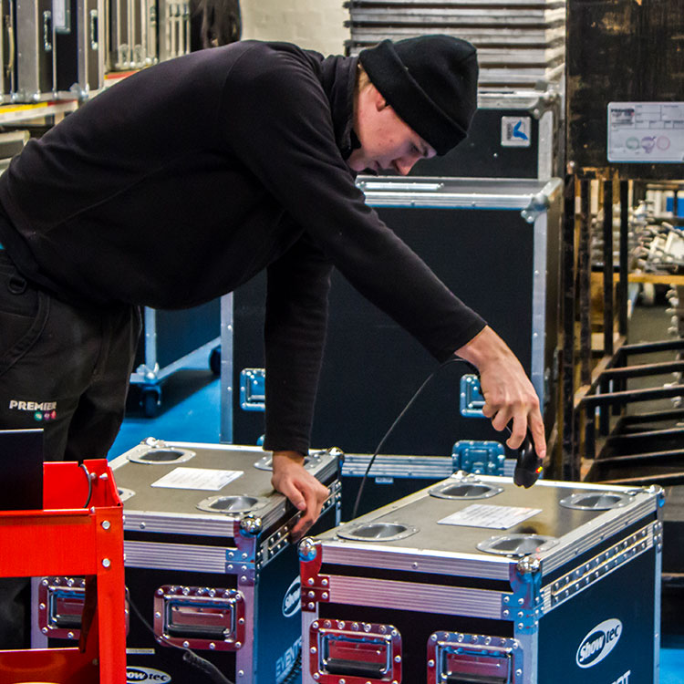 A man in a black jacket and hat diligently scans cases in an Irish warehouse.