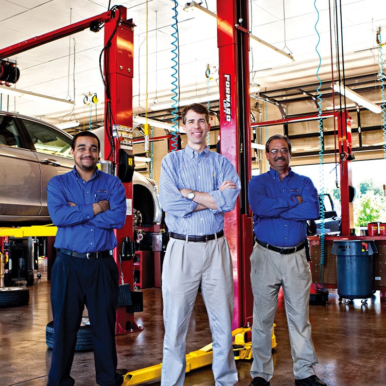Three men standing with their arms crossed in a autobody shop.