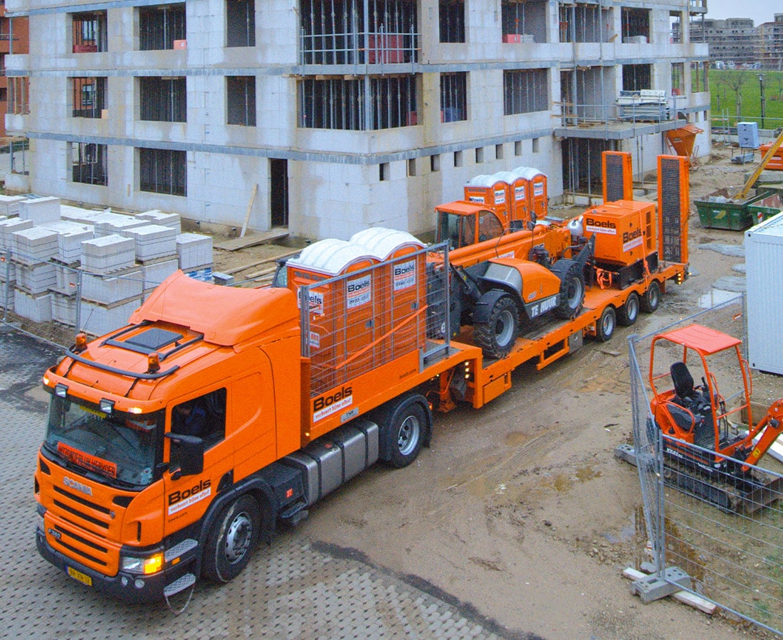 An orange truck with construction equipment on its truckbed parked in front of a building in Ireland.