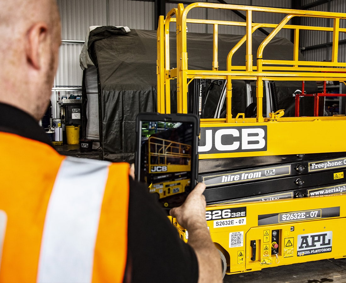 A man using a tablet to photograph a scissor lift in an Ireland warehouse.