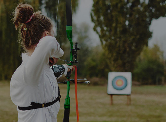 A lady with a bow and arrow aiming at a bullseye.
