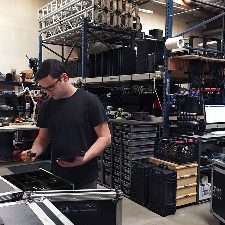 A man in an Irish warehouse, examining parts, holding a tablet, amidst shelves and equipment.