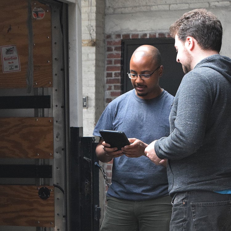 Two men standing in front of a door, engrossed in a tablet showing equipment whereabouts and status.