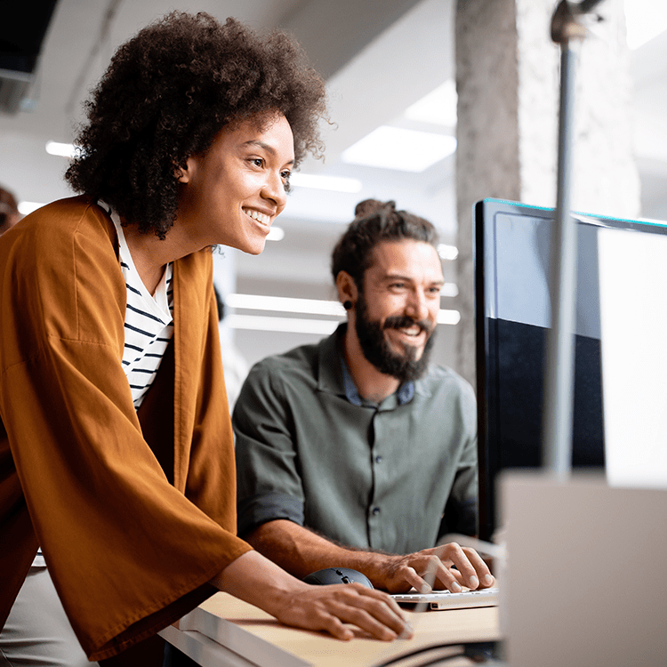 A man and woman smiling while collaborating on a computer.