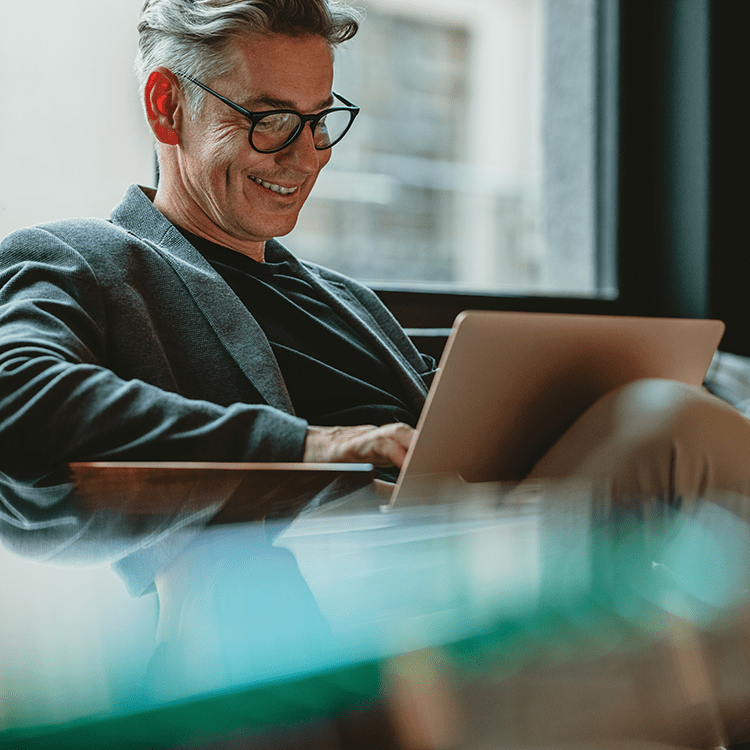 A man wearing glasses sits at a table, focused on his laptop.