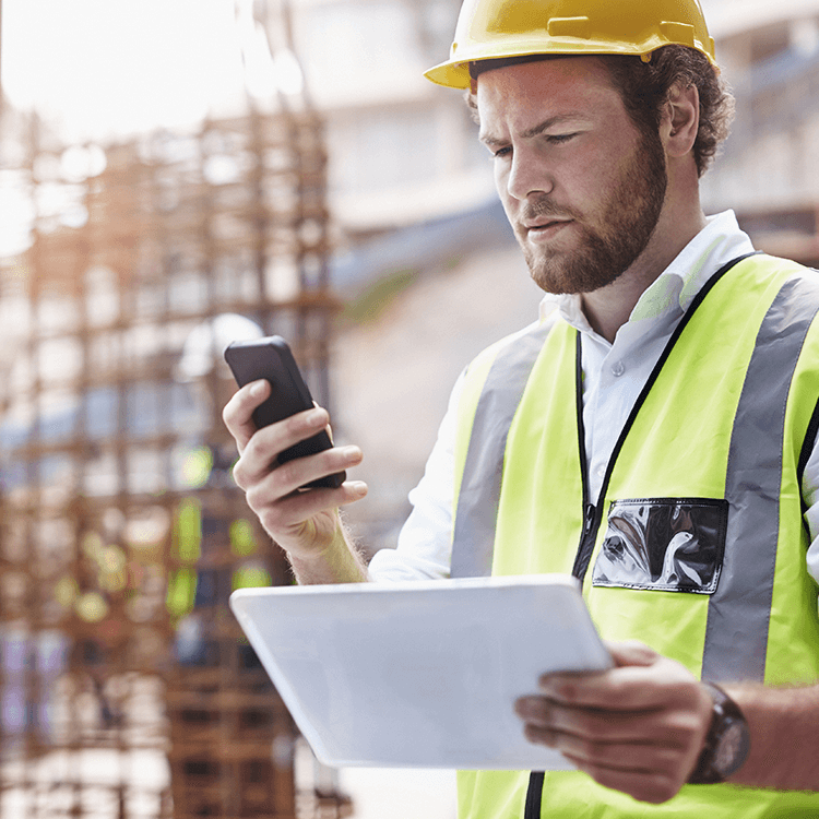A worker in protective gear holds a tablet and smartphone to access KCS's rental software.