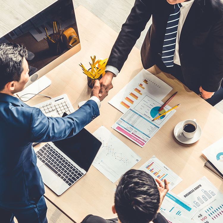  A desk meeting where three professionals shake hands, signifying a successful partnership.