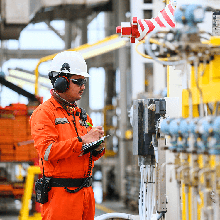 A man in an orange safety suit inspects a large industrial machine