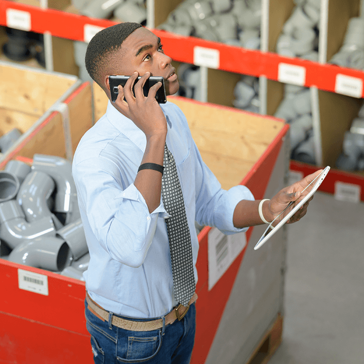 A man in a warehouse talking on a cell phone, holding a tablet