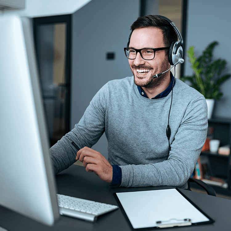 A man working in support with headphones on smiling at his desktop screen.