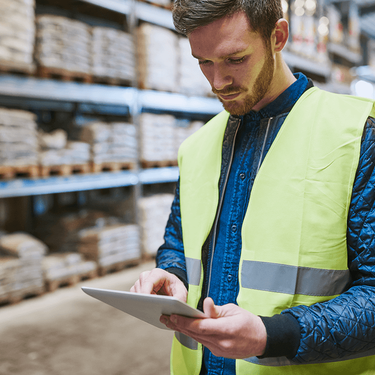 A focused professional in a vest intently using a tablet to view stock updates on their K8 ERP system