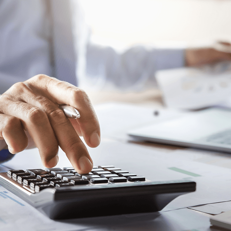 A person using a calculator, looking at business finances on their laptop.