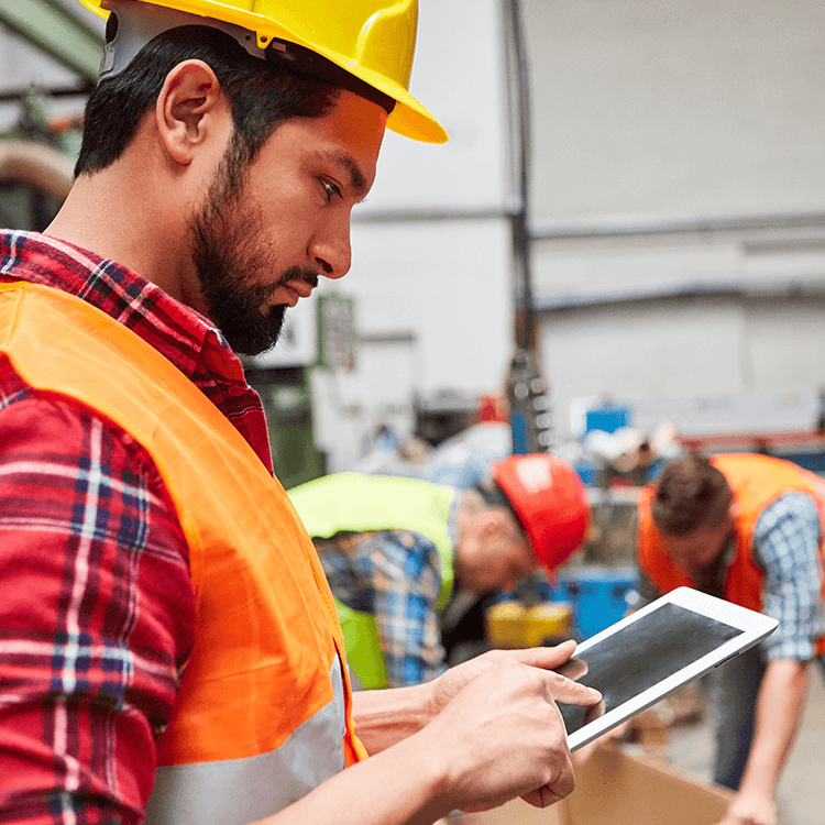 A man in an orange vest and hard hat using a tablet to perform tasks at an Irish warehouse.