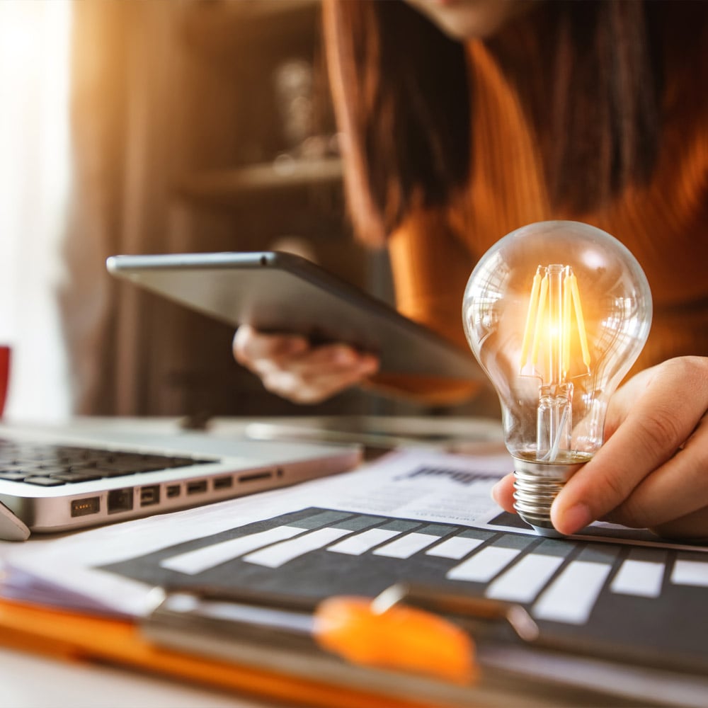 A woman working on a laptop with a light bulb nearby on a table.