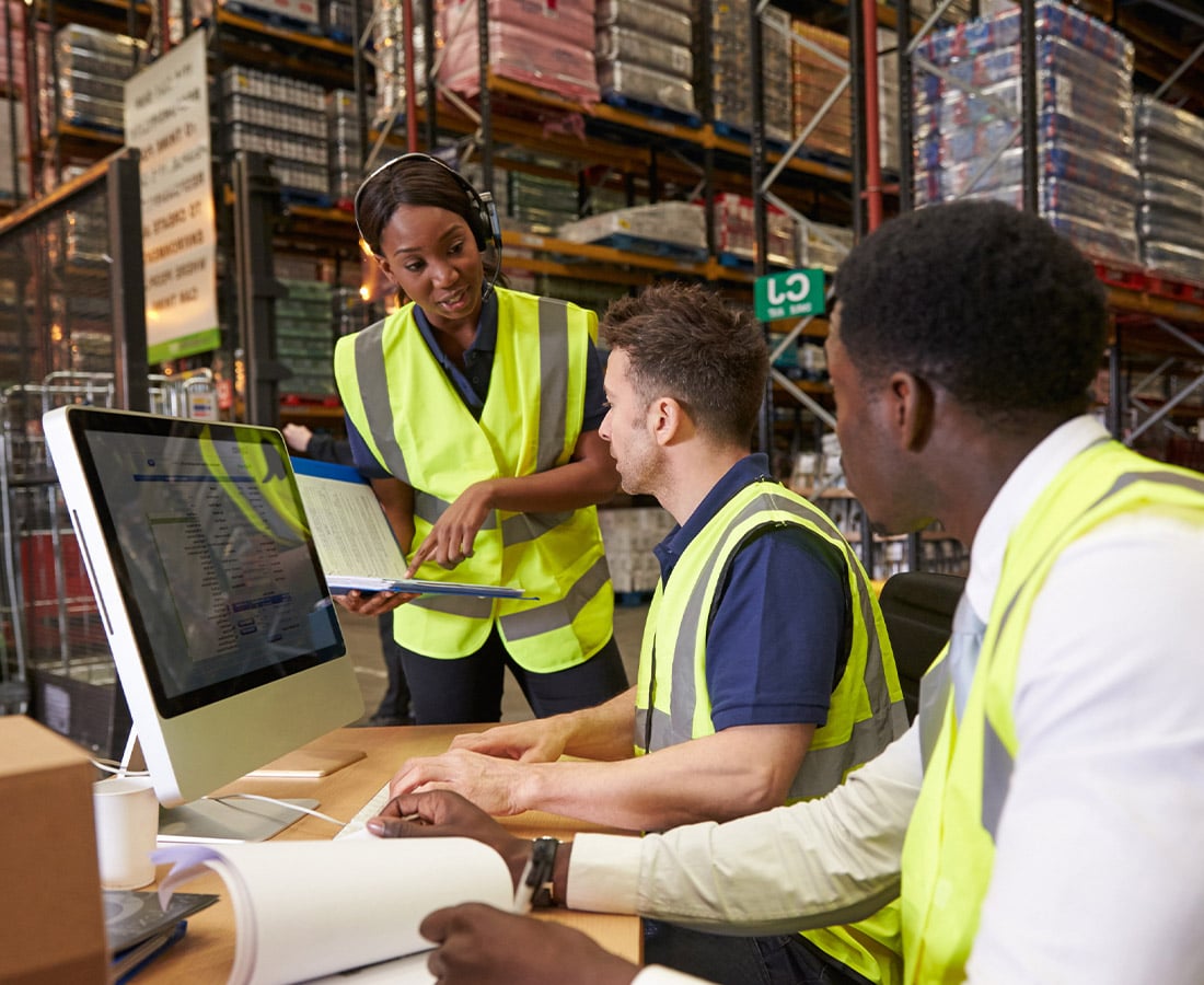 Three people in safety vests collaborating on a computer in an Irish warehouse.