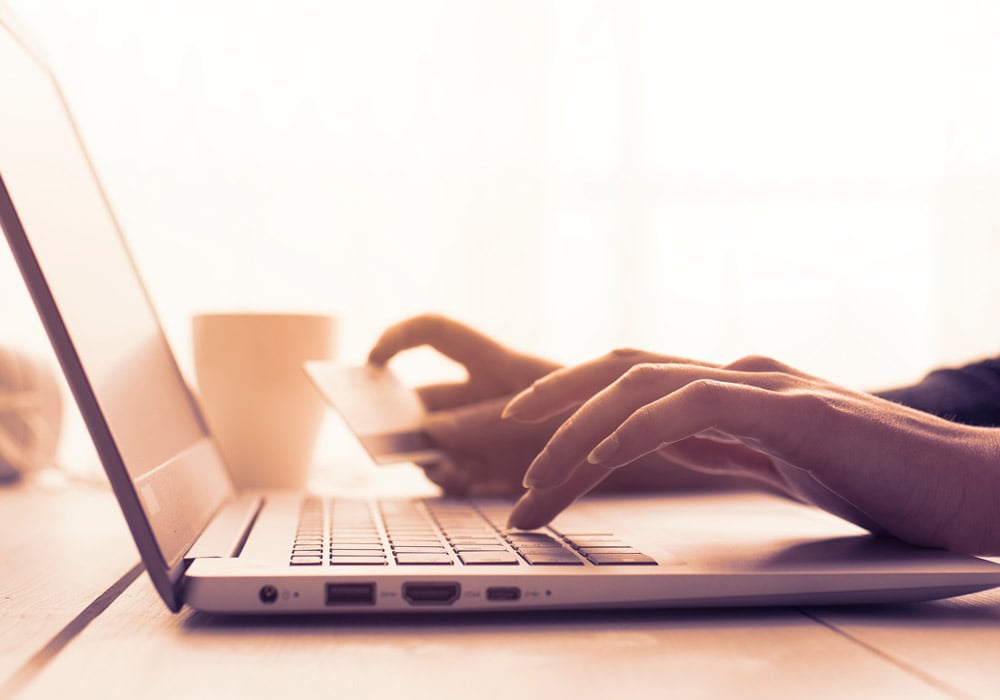 A person typing on a laptop computer with a credit card for online payment.