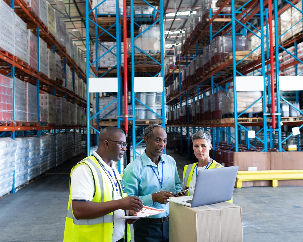 Three people working on a laptop in an Irish warehouse.