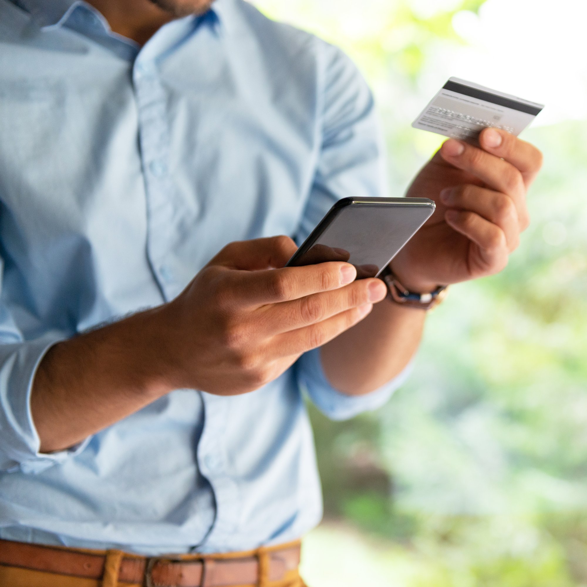 A man in an outdoor garden using a credit card and smartphone for a transaction.