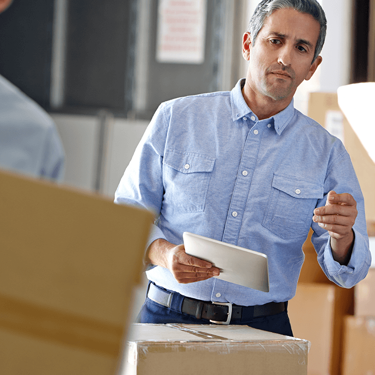 A man in a warehouse holding a tablet, overseeing tasks or managing operations efficiently.