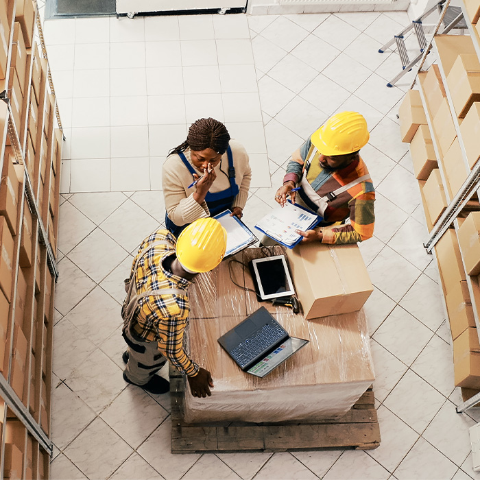 Three people wearing hard hats standing in an Irish warehouse, discussing batch control