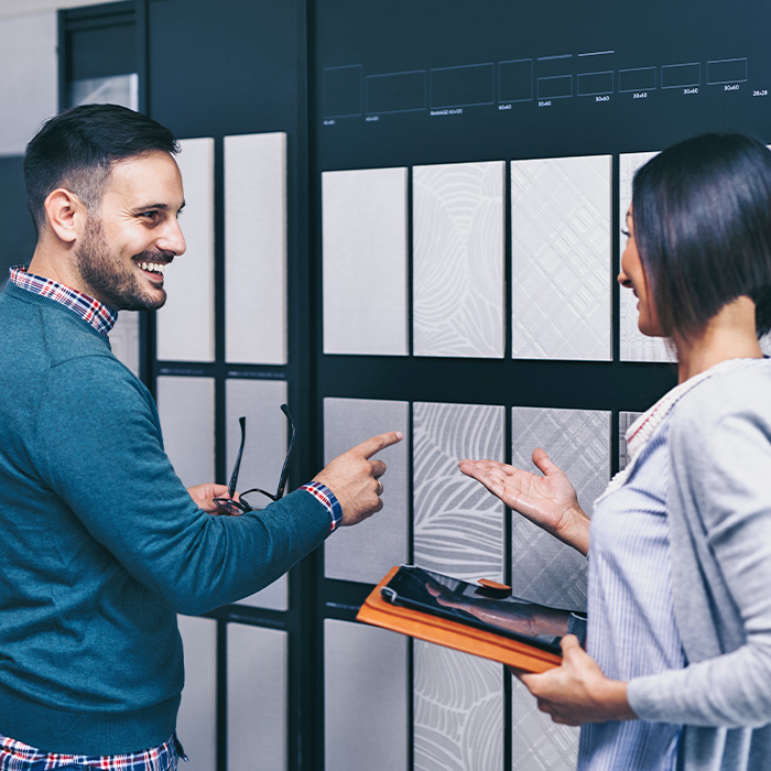 A man and woman examine a tiled wall while discussing sales order processing, holding a tablet.