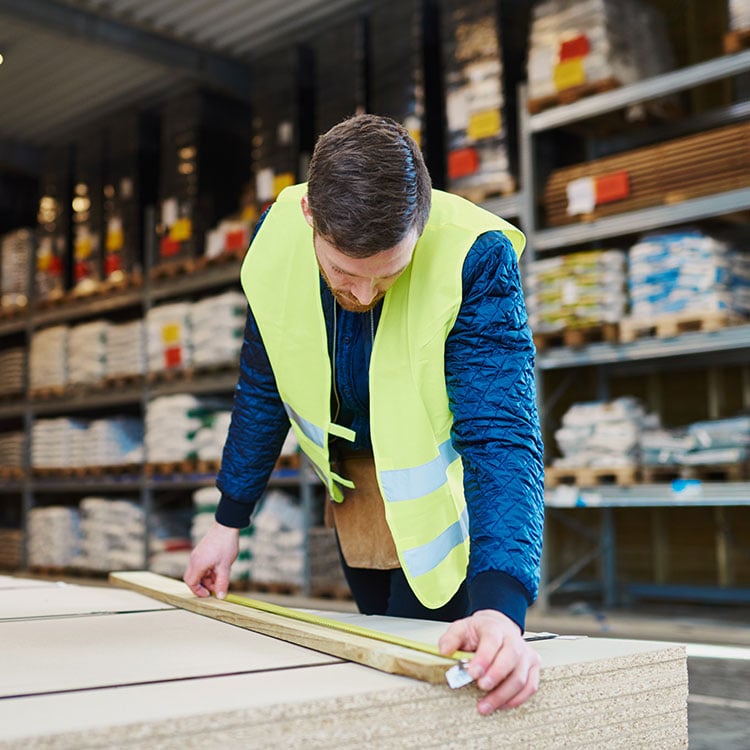 A man in a safety vest measures wood in an Irish warehouse