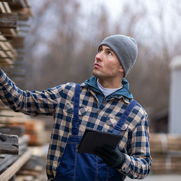 A man in overalls and a hat holds a tablet, ensuring timber margins are protected with KCS rebate functionality.