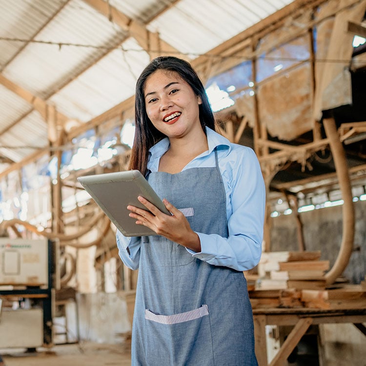 A woman in an apron holding a tablet to analyse sales.