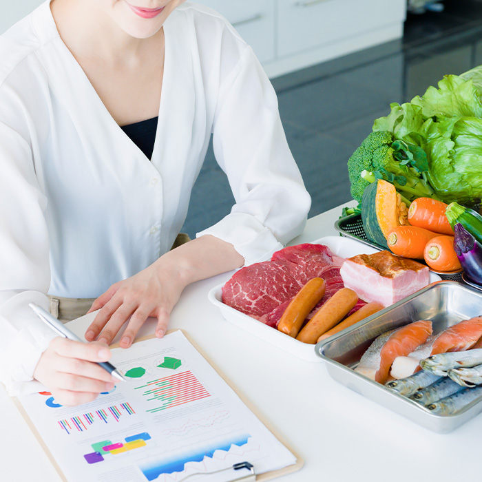 A woman writing on a clipboard with food on the desk.