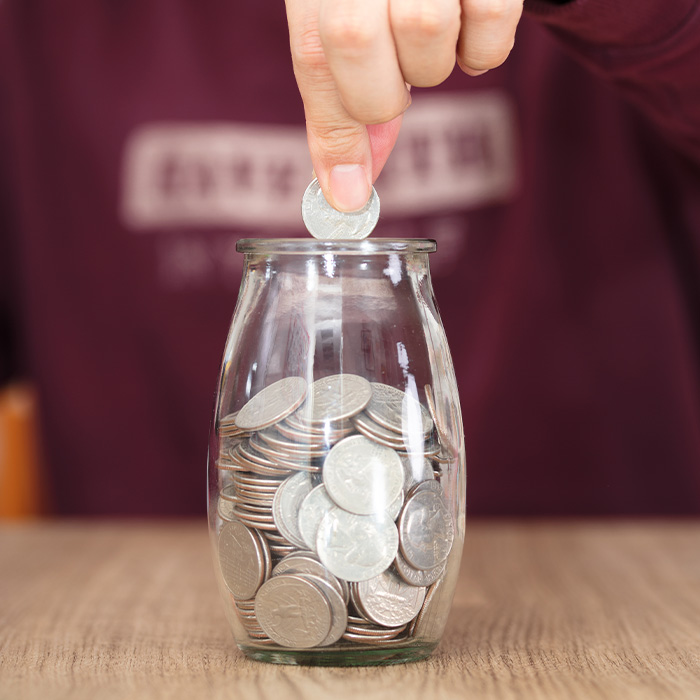 An individual putting a coin in a small jar, signifying financial management