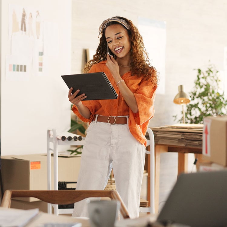 A female business owner on a cell phone looking at an ipad. 
