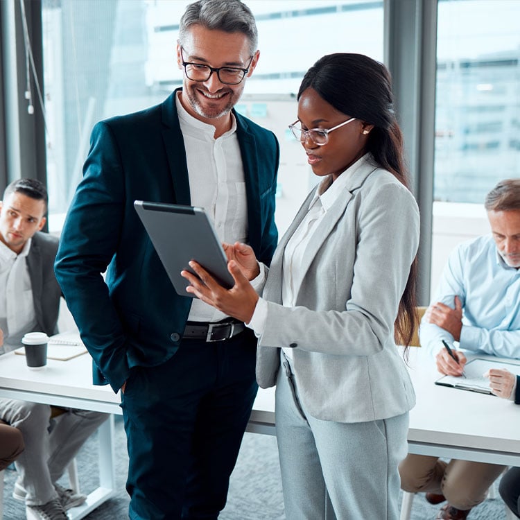 Business professionals discussing data on a tablet during a meeting in a conference room.