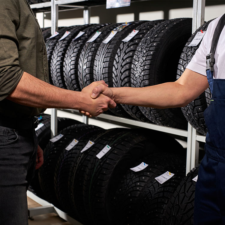 Two men shaking hands in front of tires, symbolising a successful partnership.
