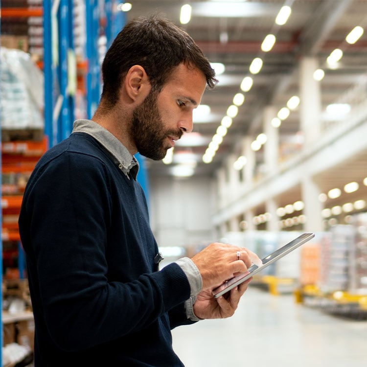 A man in an Irish warehouse uses a tablet to manage inventory and track shipments.