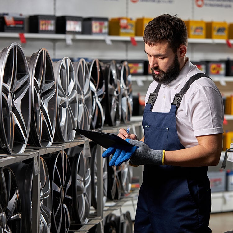 A man in an Ireland auto parts store, examining car rims, while holding a clipboard.